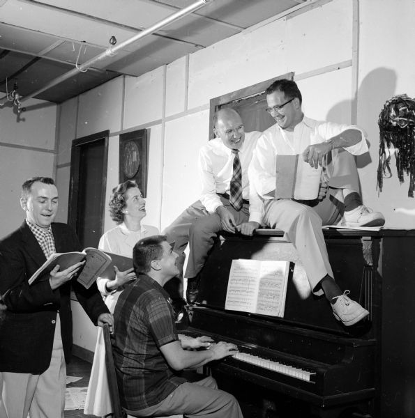 Officers of the Madison Theatre Guild frolic around a piano. Al Barraclough, director of the Guild, is sitting at the piano. The others are (left to right): Jack Davis, secretary; Louise Henning, treasurer; and on top of the piano are Jerry Dame, president; and Ralph De Sha, vice-president.