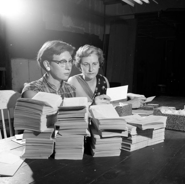 Two women are sitting behind piles of printed bulletins and a typewriter, woring at addressing each one. Jane Gintz (right) was Madison Theatre Guild's box office chairman and Clarabell Schweppe (left) was her assistant.