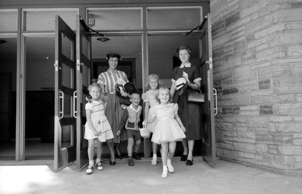 Departing St. Bernard's Catholic School located at 2450 Atwood Avenue, after a morning class session are: on the left, Mrs. Ray Kowalsky (of 106 Cumberland Lane) with her 1st-grade daughter, Kathleen, and son, Tom, not yet in school; and on the right, Mrs. George R. DeVoe (of 4800 Midmoor Road) with her 2nd-grade daughter, Kathleen, and daughter, Nancy (in the foreground), not yet in school.