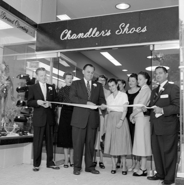 Ribbon cutting at the grand opening of Chandler's Shoes located at 10 West Mifflin Street. The salesmen have carnation boutonnieres in their coat lapels.