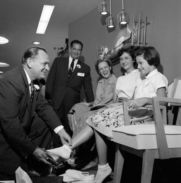 Girl being fitted for new shoes at Chandler's Shoes, located at 10 West Mifflin Street, on the first day of business. The salesmen have boutonnieres in their coat lapels. 