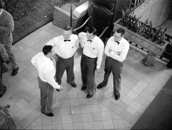 Elevated view of Tony Juisto (left), bell captain at Hotel Loraine, giving instructions to three university students working part-time as bellboys. Standing in the lobby, the students are Richard Gervais, Don Wink, and Ray Klettke.