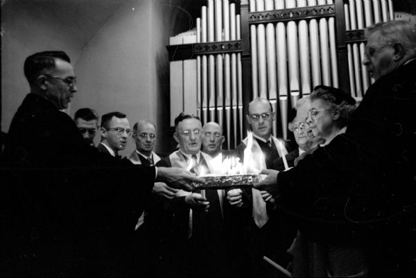 Participants with lit candles in a mortgage-burning ceremony at Trousdal Methodist Church located at 1125 Vilas Avenue, include Rev. R.D. Robinson (pastor of Trousdal Church), Rev. R.D. Clifford Northcott (Bishop of the Wisconsin Conference), and members of the congregation.    