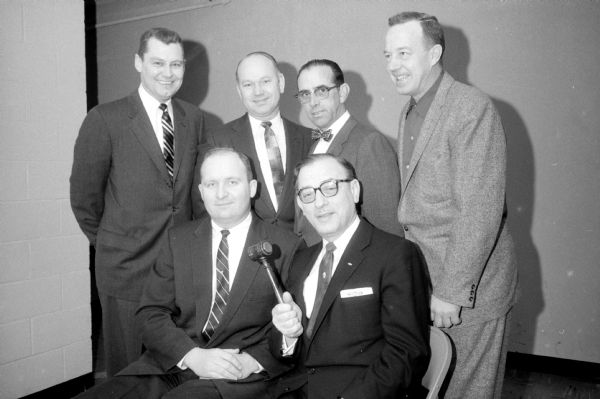Group portrait of the outgoing board president of the Madison Real Estate Board with his successor and other newly installed officers.   Seated are Robert Keller, outgoing president (left) and Philip L. Siegle, new president (right) holding a gavel. Standing (left to right) are Ben Opit, Arnold Wake, Lester Higbie and Hamilton Clark. 