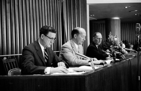 Madison City Council holds its reorganization meeting in the new City-County Building Council Chamber. Shown from left to right are City Clerk A. W. Bareis, Mayor Ivan A. Nestingen, and City Attorney Harold E. Hanson. There are many microphones in front of these council members, one for WMFM radio broadcasting the proceedings live.