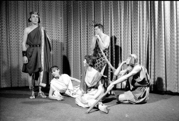 Madison Women's Club presents an original play "Man and His God" to raise money for scholarships. A group from the First Congregational Church presents a Greek vignette depicting the first form of drama about the sorrows of gods and men. Shown (left to right) are: Larry Schmitt of 1221 Milton Street, playing Orestes; Mrs. Edward Ladenburger of 103 N. Butler Street; and Mrs. and Mr. Douglas Jameson of Route 2, playing revelers. Standing in back is Edward Ladenburger playing a reveler. 