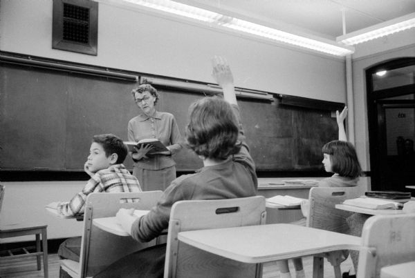 In a staged elementary school classroom scene, a teacher notices an inattentive boy.  The four actors are: Geoffrey Rotwein, Faye Daley ("teacher"), Marion Morgan, and Judy London.
