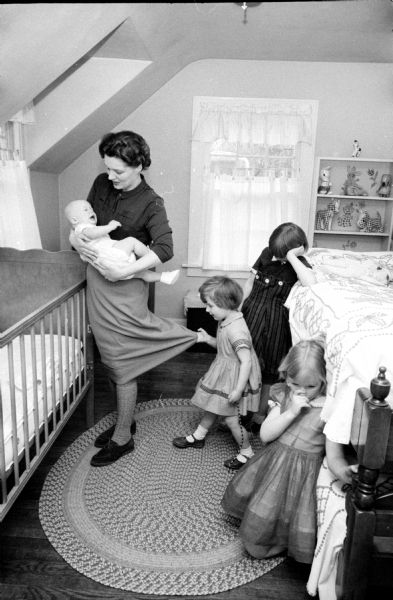 A mother and her four children enact a mental health situation revolving around stress in motherhood, raising a family, and sharing living space. The caption reads: "The eldest child resents her mother's concentration on the baby, the displaced youngster tugs at Mother's skirts, and the third child sucks her thumb in a return to her own babyhood. Mental health problems arise from childhood rivalries. Early treatment can correct most difficulties, but the best mental health safeguard is prevention."