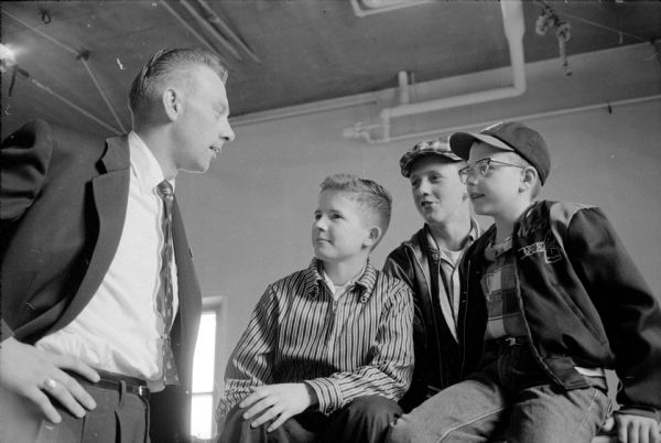 Three <i>Wisconsin State Journal</i> carriers entered in a magazine subscription contest get a pep talk about getting subscriptions from Bob Neuendorf, a district manager. The boys are Bill Kuehn, Richard Cunningham and David Lee.