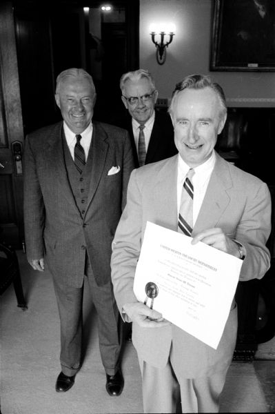 Wisconsin Governor Vernon W. Thomson (right) is presented with a certificate naming him honorary chairman of the Wisconsin Savings Bond Division of the U.S. Treasury Department. Looking on are (left to right): Harold Dickens, U.S. Treasury Department (of Washington D.C.) and James J. Callan, Savings Bonds Division (of Milwaukee).
