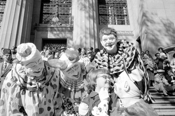 Four Zor Shrine clowns entertain young girl Mary Farmiloe during the annual spring ceremonial at the Masonic Temple. The clowns are (left to right): Tom Rogers, Horace Johnston, Leland Shaw, and Roy Tetzlaff. The group is on a set of stairs in front of temple. 