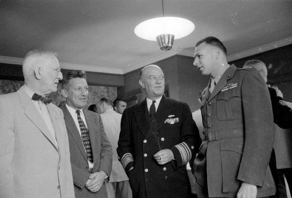 At the reception, the Washington official is shown talking with Madison armed forces. Standing left to right are: Harrison L. Garner, supervisor of the State Department of Veterans Affairs and Armed Forces Day parade marshal; Lt. Col. A.C. Smith, Wisconsin Air National Guard; and Maj. Robert I. Perina, Commandant of the Marine Reserves unit in Madison.