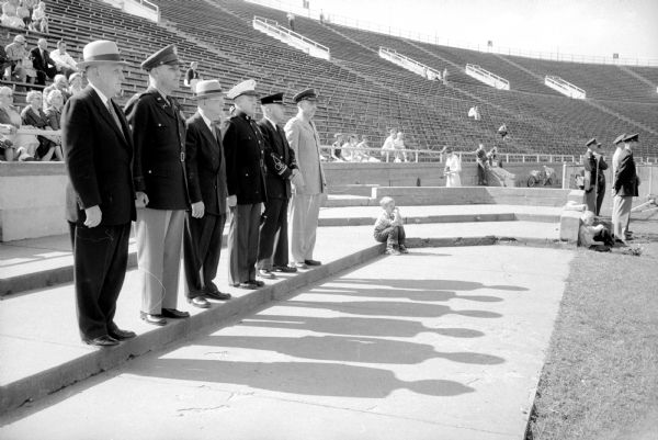 Six official reviewers at the ROTC review at Camp Randall stadium. Left to right are: U.W. President E.B. Fred; Col. Chester Allen, Army ROTC; U.W. Vice-President Ira A. Baldwin; Marine Col. Douglas Reeve, Navy ROTC; U.W. Bands Director Ray F. Dvorak; and Col. I. Freiburger, Air Force ROTC. A youngster is sitting on the turf at the reviewers left.