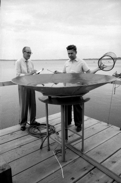 Dr. Theodore Schreiner, a research assistant from Tuebingen, West Germany (right), holds a cage while Laboratory Director Professor Arthur D. Hasler records data during an experiment with fish at the U.W. Hydrobiology Laboratory on Lake Mendota.