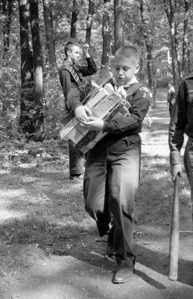 Gene Maddrell carries firewood for the fire pit where the scouts are building a fire to cook their lunch of hot dogs and buns with baked beans at Hoyt Park. The boy next to him has a baseball bat in his hand.