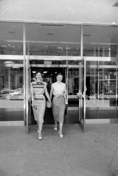 What do typical Madison female office workers do on their lunch break? A reporter accompanied two workers from the City-County building to find out. Doris Ardelt (left), who works at the civil defense office, and Joal Fenn, who works in the personnel department, are shown leaving the building at lunch time.