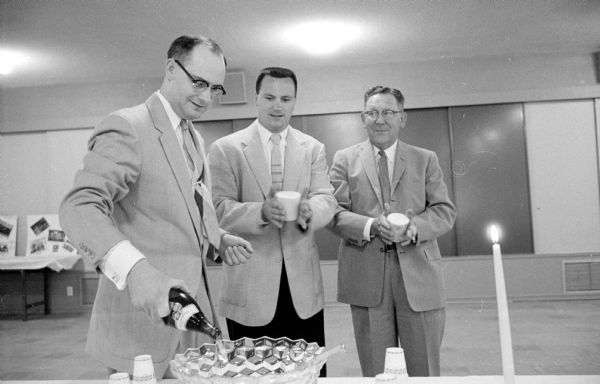 Dr. George Heathcote, chairman of the event, is filling the soft-drink punch bowl at the retirement party for retiring general secretary of the Madison YMCA, Loren Cockrell, at Camp Wacanda. Waiting for a sample are Jim Pahlmeyer, Camp Wacanda director, and Lester Emerson (right).