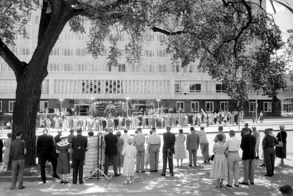 View of the dedication event of the new $8.6 million City-County Building in Madison from the sidewalk across the street on Monona Avenue (now Martin Luther King Jr Boulevard). Crowds line the sidewalks on both sides of the street.