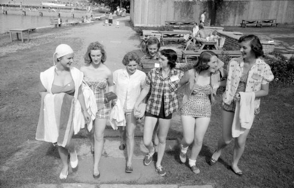 Summer music camp participants shown coming from a swim on the University of Wisconsin campus. The teenagers are (left to right): Kay Halverson (of Menasha); Karen Gosh (of Elmhurst, IL); Bonnie Jacoby (of Saukville); Pat McGinnity (of Argyle); Bernadette Bolger (of Minoqua); and Nana Kurtz (of Two Rivers). In the background is Marcia Miller (2910 Waunona Way, Madison).
