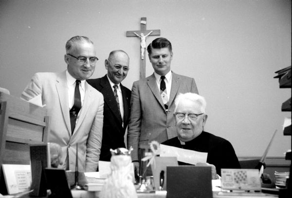 Representatives of the Wisconsin Catholic Order of Foresters present a $1,000 check to Madison Diocese Bishop William P. O'Connor. The funds will be used to aid students studying for the priesthood. Standing behind the Bishop are (left to right): Reinold J. Klein (Sun Prairie), State Chief Ranger; E.A. Lins (Spring Green), State Trustee; and Ronald W. Bartol (Beaver Dam), field representative. A crucifix is hanging on the wall behind them. 