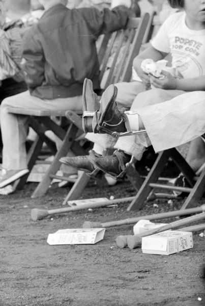 A handicapped child is enjoying the Shrine-Knights of Columbus benefit show at Breese Stevens Field. Her crutches are laying beside her chair. Her T-shirt is for "Popeye Pop Corn," and boxes for the snack are on the ground.
