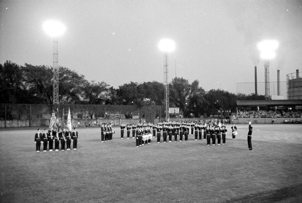 Madison Scouts Drum and Bugle Corps at the Shrine-Knights of Columbus benefit show are performing in the middle of Breese Stevens Field. The stadium lights are on at the perimeter.
