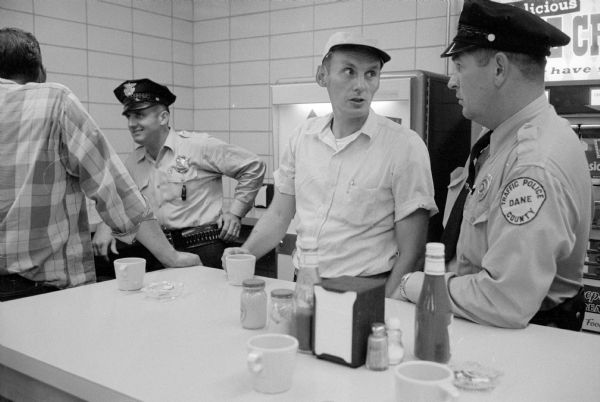 Employees of the new City-County Building enjoying refreshments in the canteen. Center, Dane County Sgt. A.M. Amble is talking with Patrolman, George Hughey. In the background, city police Patrolman Randall Perko visits with a friend.
