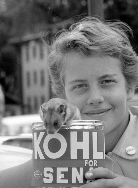 Dorothy Honeck (11), daughter of State Attorney General Stewart Honeck (of 714 Oneida Place), with her pet hamster and a poster for U.S. Senate candidate Walter J. Kohler. Dorothy participated in a campaign caravan for Kohler touring Dane County. She is holding a can with "Kohler for Senator" on it, and is wearing a button on her collar that reads "Kohler".