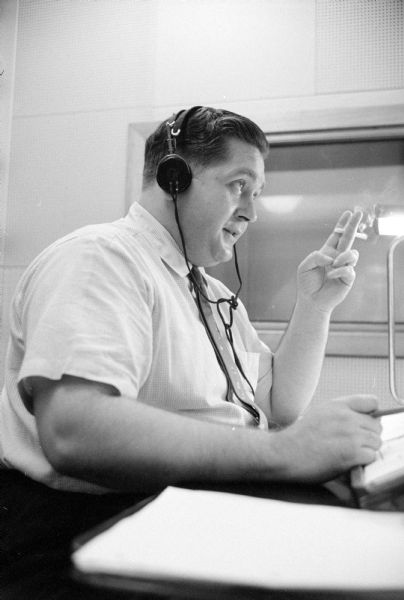 Chuck Moffett, a disc jockey at WKOW, spins vinyl records on his show "Music with Moffett" and other programs. He is wearing headphones and is holding a cigarette.