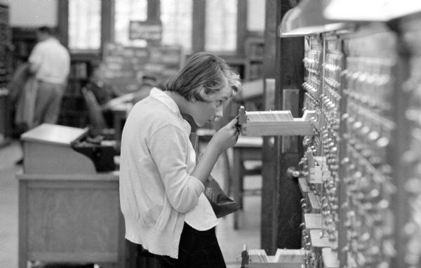 A young woman is peering into a drawer of the card catalog of the Madison Public Library.
