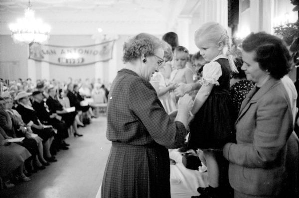 The national Women's Christian Temperance Union (WCTU) holds their annual convention at the Hotel Loraine. Mrs. Fred J. Tooze (of Portland, Oregon), WCTU national recording secretary, places a white ribbon around the wrist of Beth Towner (age 4) as a symbol of her dedication to total abstinence. Beth's mother Mrs. Robert Towner (1806 Vilas Avenue) looks on.       