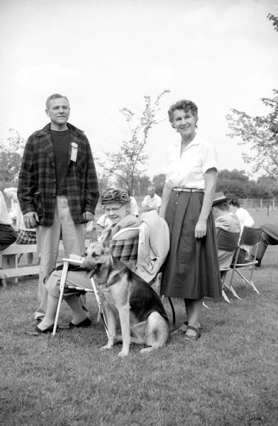 Participants in the 4th Annual Dog Obedience Trials held at the Double A Arena near Cambridge. Shown standing are Mr. and Mrs. Ralph Hough, Stoughton, and sitting is Mr. Hough's mother, Mrs. Susan Hough (Oak Park, Ilinois). Ralph's German Shepherd, Wendy, sits at attention.  