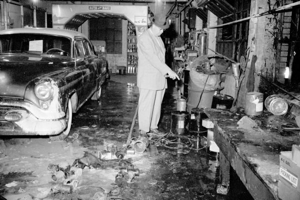 Coroner Michael Malloy standing inside the blast-damaged Pyramid Motors garage at 434 West Gilman street and pointing at a paint can and hot plate that caused the explosion. The blast killed business owner Leroy Banks, 33, of 1836 Baird Street. The incident was witnessed by his wife, Ollie, and two young sons. Ollie Banks and John O'Connor suffered burns during a rescue attempt.