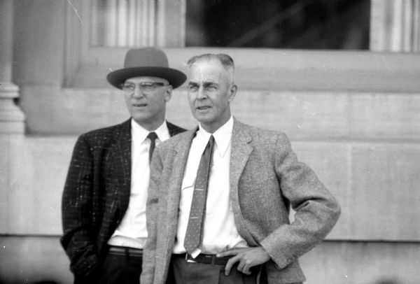 Two busy Madison lawyers pause to watch the demolition of buildings on Madison's Capitol Square to be replaced with a new building to house a J. C. Penney store. They are Assistant City Attorney Alton S. Haessler (left) and Sverre O. Braathen, Dane County divorce counsel. The photograph was taken with a new telephoto lens.