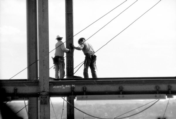 Steel construction workers are standing on exposed beams for the new constriction of the West Tower of the Wisconsin State Office Building at 1 West Wilson Street. The men are wearing hard hats and tool belts.   