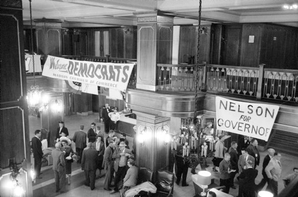 Elevated view of delegates beginning to arrive at the State Democratic Convention held at the Hotel Loraine. Approximately 2,000 delegates are expected to attend the convention. Signs hanging from the second floor over a crowd in the lobby read: "Nelson for Governor" and "Wisconsin Democrats."