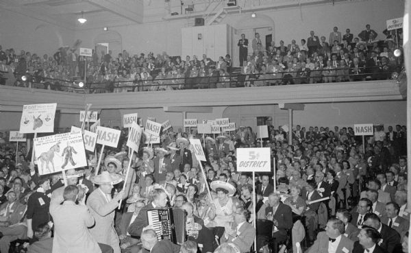 The biggest demonstration of the second day of the State Democratic Party Convention at the Central High School auditorium for Philleo Nash of Wisconsin Rapids. Nash, the incumbent, opposed Patrick J. Lucey for the chairmanship of the Democratic Party, but Lucey won the election by a close vote of 692-687. One man in the crowd is playing an accordion and others are holding political signs.