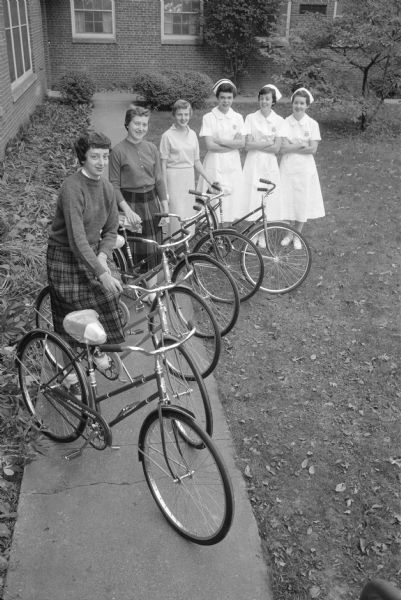 Student nurses at Madison General Hospital standing with bicycles received from the hospital's medical staff as a gift for Student Nurses Week. Shown (left to right) are student nurses: Beverly Hofland (DeForest); Karen Thompson (Portage); Kay Temte (Reedsburg); Carla Horlamus (2546 Fairfiled Place); Margaret Owen (Viroqua); and Alice Linse (Eau Claire). Some are in uniform with their nurses caps.