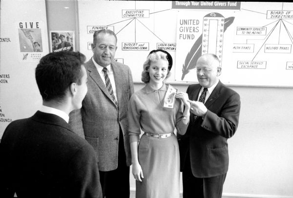 Miss Wisconsin, Joan Hentchel, is named Miss Red Feather by the Madison United Givers' Fund. She is shown receiving the award from campaign chairman Charles N. Goulet (right), and L.W. Lackore (left), master of ceremonies for the fund report meetings. She is congratulated by William Luebke (222 Lake Lawn Place).
