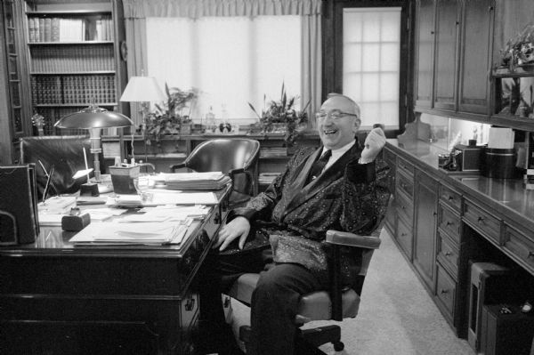 Dr. Schindler at home sitting at his writing desk in his library and study. The caption says he is wearing a deep red silk smoking jacket and that he took a two-month leave of absence from his medical practice to write his book, <i>Woman's Guide to Better Living 52 Weeks a Year</i>." The doctor was killed in an automobile accident on November 16.