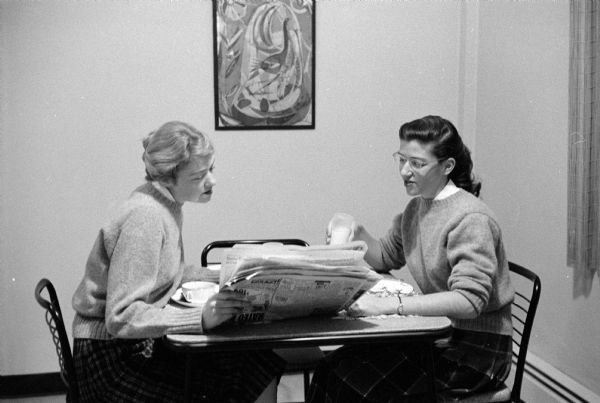 Two Schindler daughters, Dora (23, left) and Elsa (21) are shown sitting at a table examining their father's second published book, <i>Woman's Guide to Better Living 52 Weeks a Year</i>.  The book ran in condensed form with 12 installments in the <i>Wisconsin State Journal</I>. Dora taught at Marquette School in Madison and Elsa was a senior at the university.
