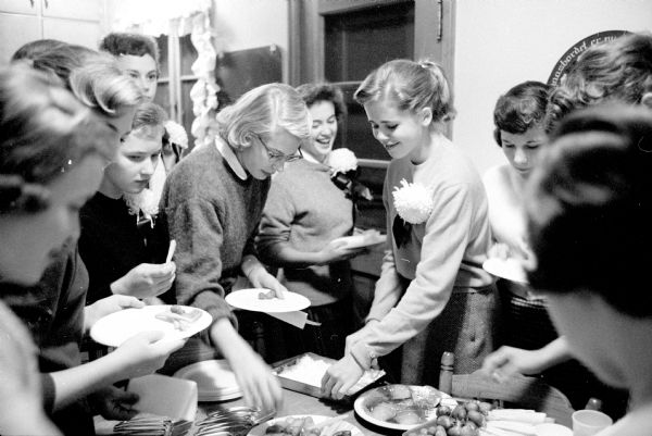 Edgewood High School girls help themselves to food at a potluck before the school's football game. The potluck was at the home of Mark and Mary Schmitz and hosted by their daughter, Martha. Some girls are wearing chrysanthemum corsages for the occasion.