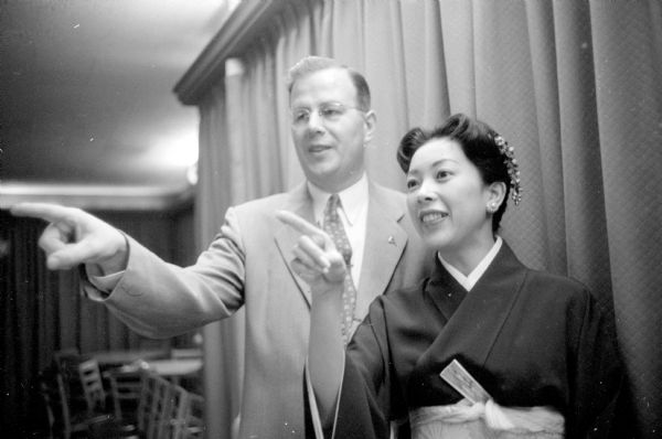 Actress Muko Taka with Sertoma Club President, Don Jensen. She was a guest at the Club during a visit to Madison, when performing in the play "Sayonara" at the Capital Theater in December. She is wearing a kimono and a fan is tucked into her obi. Her hair is pinned with a traditional decorative comb.