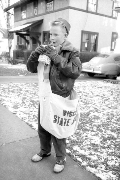 13-year-old Phil Shuler, son of Mr. and Mrs. George Shuler, and carrier for the <i>Wisconsin State Journal</i>, is shown delivering envelopes for donations to the Empty Stocking Club along with the newspapers. The envelopes are then filled and returned to the carrier or mailed to the State Journal office. Phil, an 8th grade student at West Junior High, earns $9.50 a week and intends to give part of his earnings to this charitable cause as well.