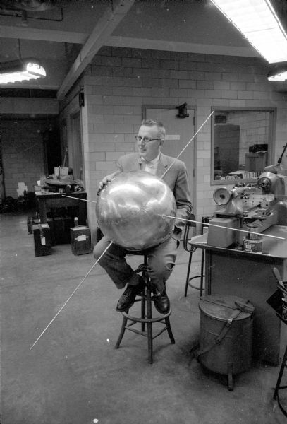 Professor Verner Suomi of the University of Wisconsin meteorology department and leader of a university team building one of the U.S. satellites, is shown in his lab holding a full-scale model of the Vanguard satellite. Suomi of the meteorology department led a team that constructed instruments that were to be included inside one of the U.S. Vanguard satellites. Suomi hoped to study the flow of heat from the Sun to the Earth and then back to space.