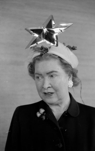 Mrs. George W. Heath, 1957 social chairman of the woman's organization at Maple Bluff Country Club, is wearing a hat decorated with a large Christmas tree star.