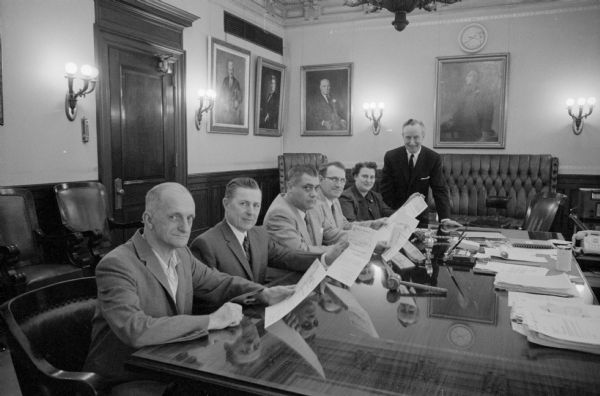 Five state employees are recognized for contributing ideas to save the Wisconsin state government money. They are receiving merit certificates and cash awards. Shown with Governor Vernon W. Thomson (standing) are (left to right): Henry T. Roger, Rt. 2 Madison; Peter C. Rortveck, Middleton; Anthony LaMalfa, Milwaukee; Fritz Johnson, Boscobel; and Mrs. Carol Bussian, 417 Memphis Avenue.  