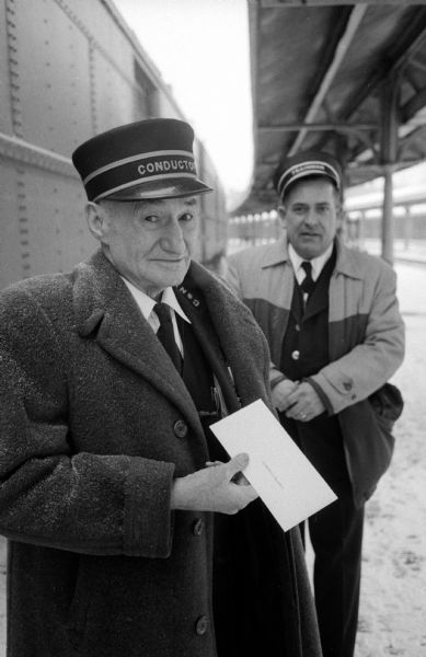 Patrick J. Donnelly (left) on his last day of work after serving as conductor with the North Western Railway for 52 years. K.M. Prenot (right), a brakeman for the railway, presented Donnelly with a gift of cash from his fellow workers. They are standing on a railway platform.