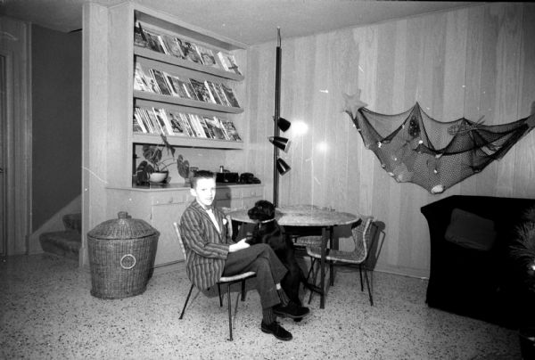 The tri-level home of I. Franklin and Arline Houseman, 821 Lakewood Boulevard in Maple Bluff, was redecorated with her choosing the color scheme. Their son Ricky Houseman is sitting with his dog in the family room that has a driftwood finish used for wall paneling. The built-in bookcase behind him serves as a magazine rack.