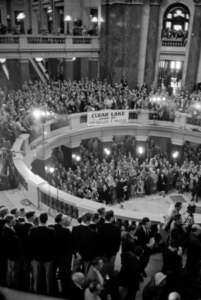 Standing audience for the inauguration of Wisconsin's new governor, Gaylord Nelson, in the Capitol Rotunda. A sign posted on the second-floor railing reads: "Clear Lake Home of Gov. Gaylord A. Nelson."